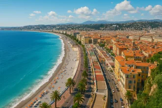 Panoramablick auf Nizza an der Côte d’Azur mit azurblauem Meer, Strandpromenade, Palmen und den typischen roten Dächern der Altstadt.