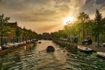 Sonnenuntergang über einer Gracht in Leiden, Niederlande, mit Booten, Bäumen und historischen Häusern am Wasser