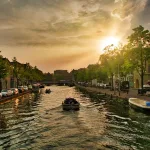 Sonnenuntergang über einer Gracht in Leiden, Niederlande, mit Booten, Bäumen und historischen Häusern am Wasser