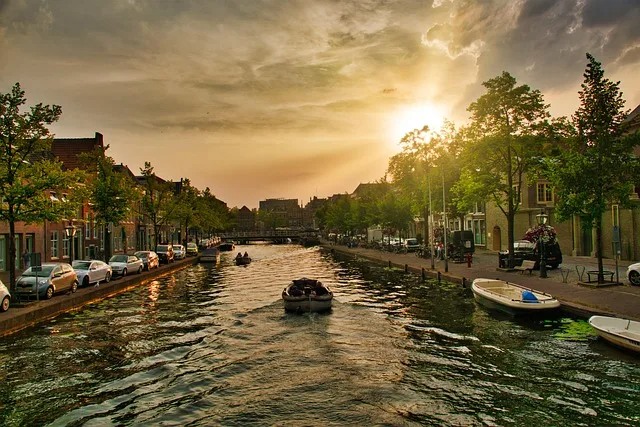 Sonnenuntergang über einer Gracht in Leiden, Niederlande, mit Booten, Bäumen und historischen Häusern am Wasser