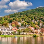 Blick auf Heidelberg am Neckar mit bunten Häusern, grünen Hügeln und strahlend blauem Himmel.