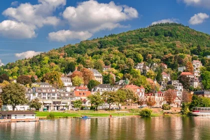 Blick auf Heidelberg am Neckar mit bunten Häusern, grünen Hügeln und strahlend blauem Himmel.