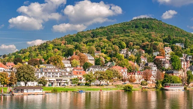 Blick auf Heidelberg am Neckar mit bunten Häusern, grünen Hügeln und strahlend blauem Himmel.