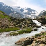 Alpiner Gebirgsbach mit Felsen und schneebedeckten Bergen im Hintergrund