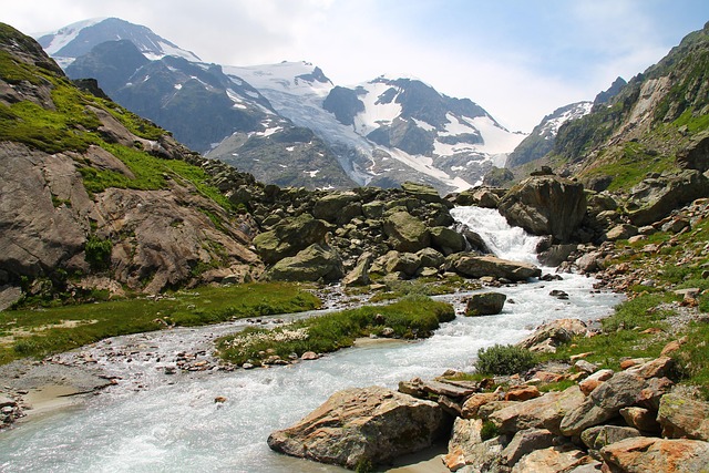 Alpiner Gebirgsbach mit Felsen und schneebedeckten Bergen im Hintergrund