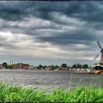 Windmühle in Zaanse Schans, Niederlande, am Fluss Zaan mit Blick auf das historische Dorf und dramatische Wolken am Himmel