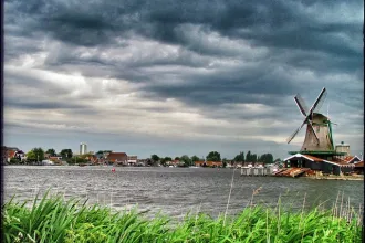 Windmühle in Zaanse Schans, Niederlande, am Fluss Zaan mit Blick auf das historische Dorf und dramatische Wolken am Himmel