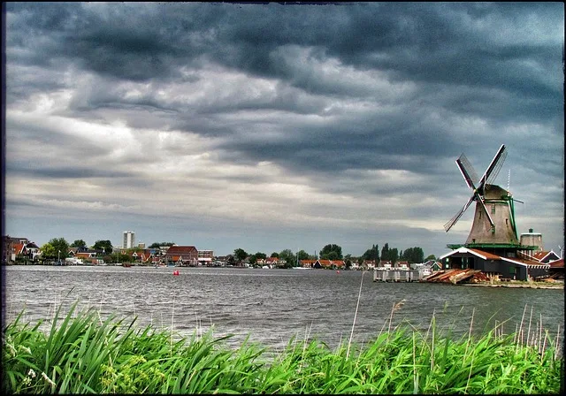 Windmühle in Zaanse Schans, Niederlande, am Fluss Zaan mit Blick auf das historische Dorf und dramatische Wolken am Himmel